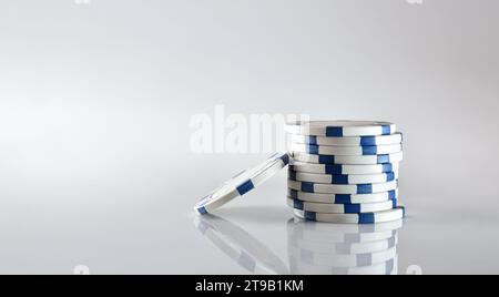 Pila di chip di scommesse bianche e blu dei giochi del casinò riflessi in un tavolo di vetro e in uno sfondo bianco isolato. Vista frontale. Foto Stock