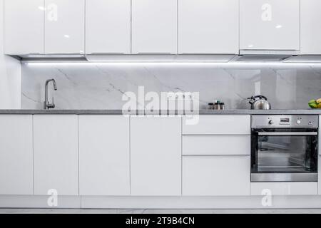 Una cucina pulita e luminosa con armadi completamente bianchi e un design moderno. L'atmosfera generale della cucina e' semplicistica, rinfrescante e invitante, mak Foto Stock
