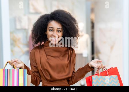 Ritratto di una donna gioiosa che fa shopping, cammina attraverso un supermercato in un grande negozio con vestiti, sorrisi e guarda la fotocamera, mostra borse colorate con regali, è soddisfatto delle vendite. Foto Stock