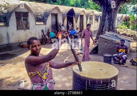 Tanzania, Kilombero - di fronte alle case delle piantagioni in una piantagione di sisal, una donna produce birra locale in una vecchia botte di petrolio. Foto Stock