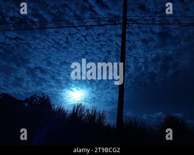 Una brillante luna piena illumina un tranquillo cielo notturno, proiettando un bagliore pallido su un lussureggiante campo erboso sottostante Foto Stock