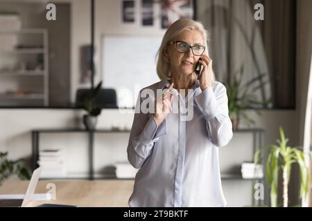 Dirigente d'affari senior concentrato donna in occhiali che parla al cellulare Foto Stock