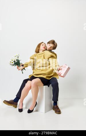 Periodo di bouquet di caramelle. Abbina gli abbracci in una giacca con mazzi di fiori e presenta sullo sfondo bianco dello studio. Foto Stock