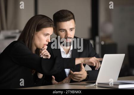 Due giovani colleghi di lavoro concentrati che lavorano al notebook Foto Stock