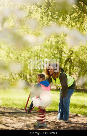 Smiling female teacher taking care of girl on playground swing Stock Photo