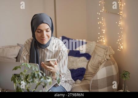 Sorridente freelance che utilizza lo smartphone mentre lavora da casa Foto Stock