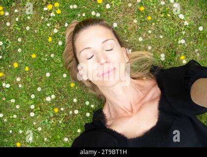 Direttamente sopra la vista di una donna sdraiata con gli occhi chiusi sull'erba Foto Stock