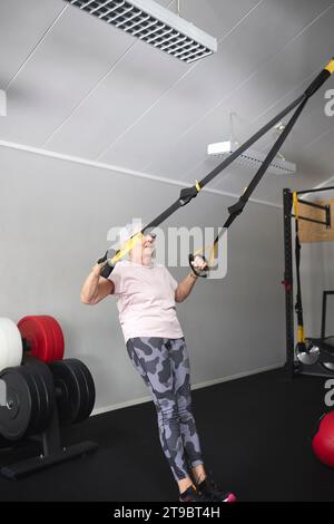 Lunghezza completa della donna anziana che si esercita su anelli di ginnastica al centro benessere Foto Stock
