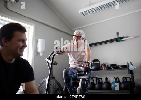Vista dall'angolo basso della donna anziana sorridente in cyclette che guarda l'uomo in palestra Foto Stock