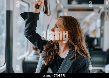 Passeggero femminile che indossa cuffie intrauricolari wireless mentre è in treno Foto Stock