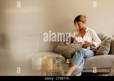 Madre che allatta il bambino mentre è seduto sul divano a casa Foto Stock