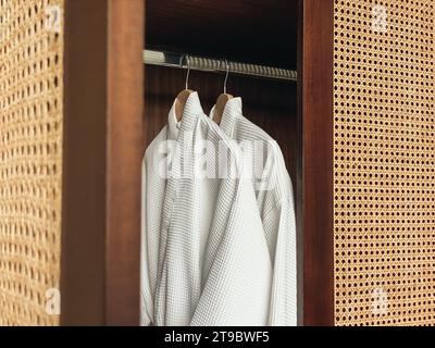 Due accappatoi bianchi e puliti appesi in un armadio di legno in un hotel di lusso o a casa. Concetto di relax e viaggio Foto Stock