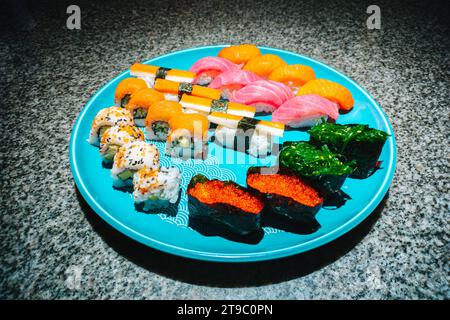 Menu giapponese di sushi e sashimi su un grande piatto blu sul tavolo in marmo Foto Stock