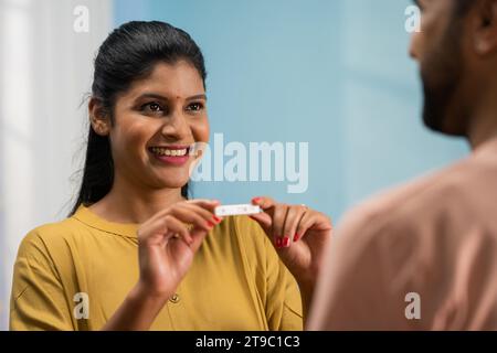 Spalla di una moglie indiana eccitata che mostra un test di gravidanza positivo al marito abbracciandosi a casa - concetto di anticipare la genitorialità, condiviso Foto Stock