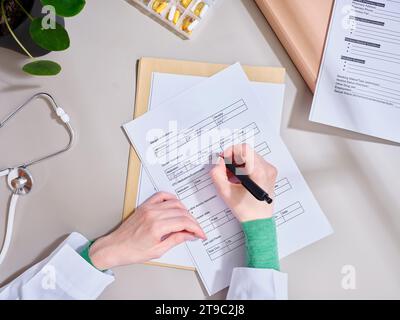 Vista dall'alto medico irriconoscibile prendere appunti nella documentazione medica presso la clinica Foto Stock