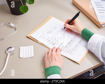 Vista dall'alto medico irriconoscibile prendere appunti nella documentazione medica presso la clinica Foto Stock