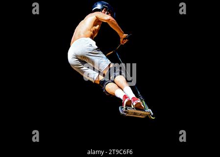 Giovane che pratica lo Scootering (Freestyle Scootering) allo Skatepark. Silhouette su sfondo scuro. Sport, gioventù, cultura urbana. Foto Stock