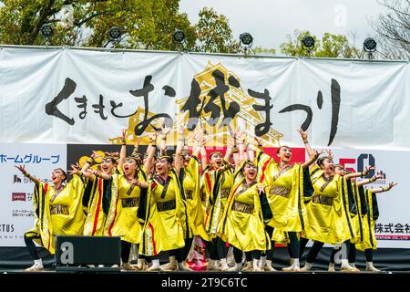 Squadra di danza giapponese di Yosakoi in costumi gialli e neri su un palco all'aperto che balla al festival annuale di Kumamoto Kyusyu Gassai. Foto Stock