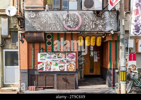 Esterno del tipico piccolo ristorante giapponese izakaya a Fukuyama. Lanterne gialle appese sopra l'ingresso e pali di bambù verdi sul muro. Foto Stock