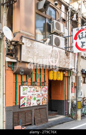 Esterno del tipico piccolo ristorante giapponese izakaya a Fukuyama. Lanterne gialle appese sopra l'ingresso e pali di bambù verdi sul muro. Foto Stock