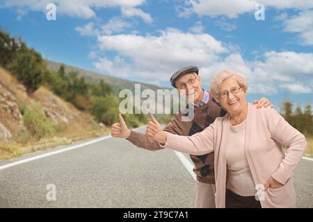 Una coppia di anziani allegri che fanno autostop su una strada Foto Stock