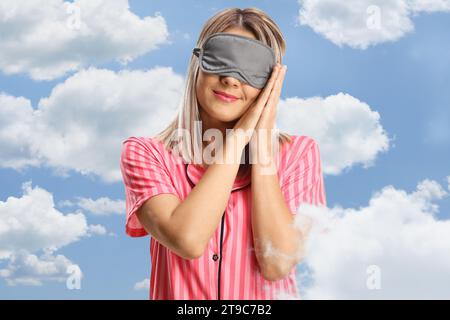 Donna in pigiama e una maschera del sonno che dorme tra le nuvole su un cielo blu Foto Stock