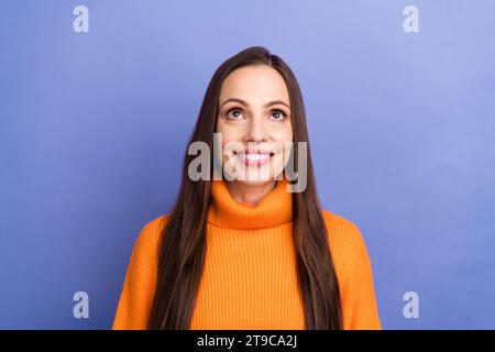 Foto di donna in età matura con maglione arancione che guarda sopra la testa idea intelligente per le future mamme risparmiare denaro isolato su sfondo di colore viola Foto Stock