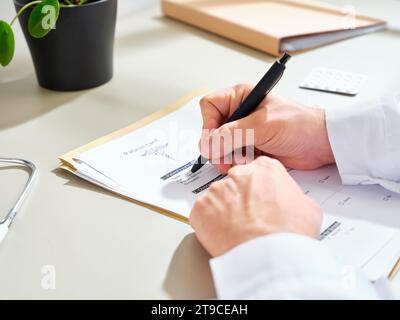 Medico maschile anonimo in un abito bianco compilando la documentazione medica in una clinica Foto Stock