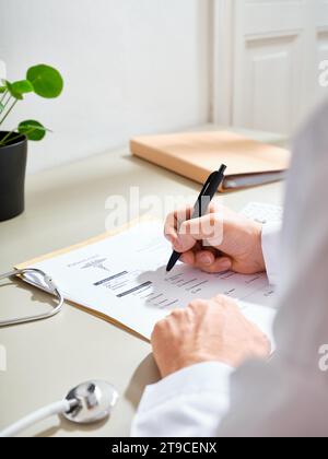 Medico maschile anonimo in un abito bianco compilando la documentazione medica in una clinica Foto Stock