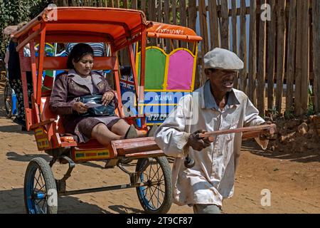 Vecchio uomo malgascio che tira pousse-pousse / risciò tirato con una donna locale in città Antsirabe, Vakinankaratra, Highlands centrali, Madagascar, Africa Foto Stock