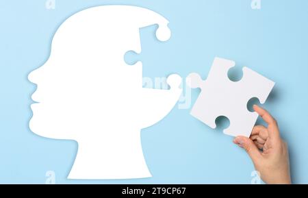 Silhouette di una testa umana che regge un pezzo di puzzle su sfondo blu, che rappresenta la salute mentale Foto Stock