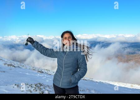 ritratto di donna latina sorridente nella neve, con abiti caldi sopra le nuvole, in cima alla montagna della sierra nevada Foto Stock