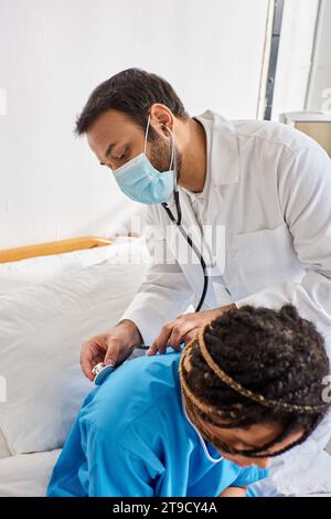 giovane medico indiano che esamina il respiro di malato paziente afroamericano con stetoscopio, assistenza sanitaria Foto Stock