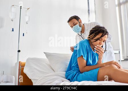 giovane medico indiano che esamina il respiro di malato paziente afroamericano con stetoscopio, assistenza sanitaria Foto Stock