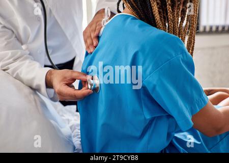 giovane medico indiano che esamina il respiro del suo paziente afroamericano con stetoscopio, assistenza sanitaria Foto Stock