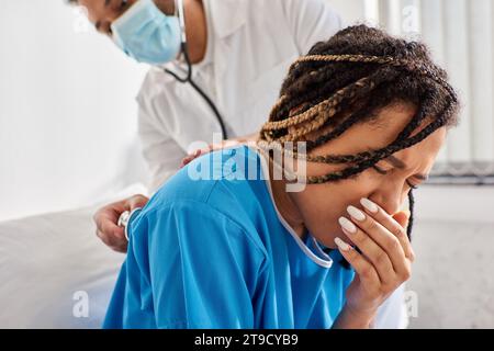giovane medico indiano che esamina il respiro di malato paziente afroamericano con stetoscopio, assistenza sanitaria Foto Stock