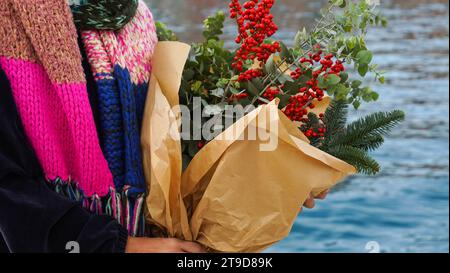 Ragazza che tiene bouquet natalizio con rami di abete, bacche d'inverno, eucalipto su fondo marino Foto Stock