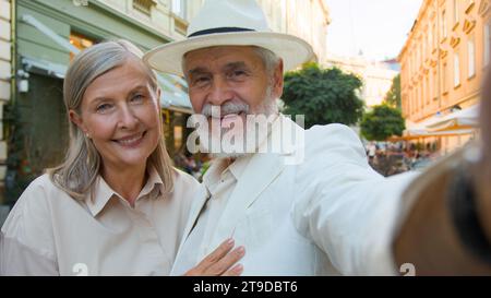Felici anziani turisti caucasici coppia uomo anziano donna che prende selfie streaming video romantico bacio telefono cellulare tecnologie moderne fuori città Foto Stock