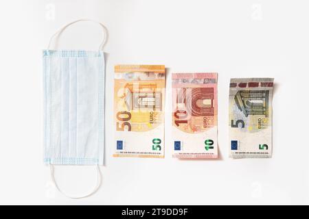 Mascherina igienica monouso e banconote in euro di diverso valore raffiguranti un grafico a barre. Concetto di crisi finanziaria risultante dopo la covid-19. Foto Stock