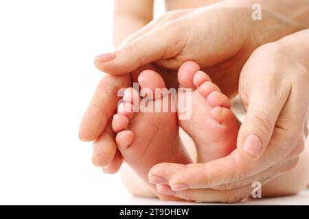 Primo piano di una madre che massaggia dolcemente i piedi e le suole del suo bambino su sfondo bianco. Foto Stock