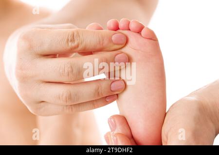 Primo piano di una madre che massaggia dolcemente i piedi e le suole del suo bambino su sfondo bianco. Foto Stock