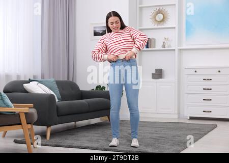 Donna che cerca di indossare jeans stretti a casa Foto Stock