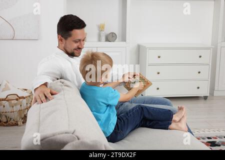 Sviluppo di competenze motorie. Padre felice che aiuta suo figlio a giocare con geoboard e fasce elastiche sul divano a casa Foto Stock