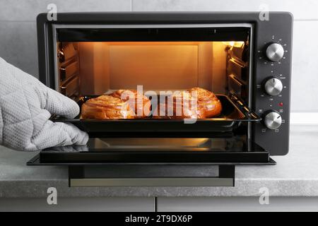 Primo piano: Donna che toglie la teglia da forno con deliziosi panini a spirale dal forno elettrico Foto Stock