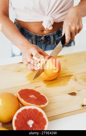 Giovane donna che taglia pompelmi sul tagliere per succhi freschi fatti in casa Foto Stock