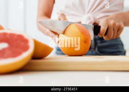 Giovane donna che taglia pompelmi sul tagliere per succhi freschi fatti in casa Foto Stock