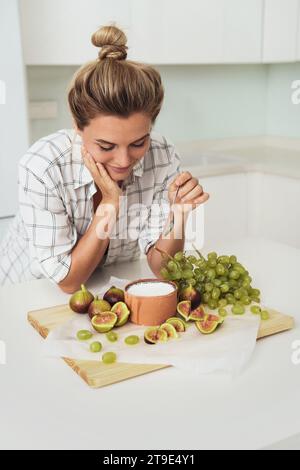 Giovane bella donna pronta a mangiare il suo delizioso yogurt greco con i fichi in cucina bianca Foto Stock