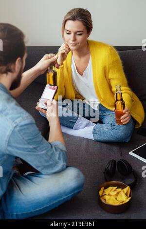Giovani coppie che bevono birra e mangiano nachos a casa Foto Stock