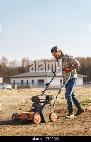 Giovane che utilizza una macchina per aerazione per scarificare e aerare prati o prati Foto Stock