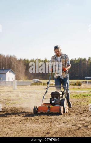 Giovane che utilizza una macchina per aerazione per scarificare e aerare prati o prati Foto Stock